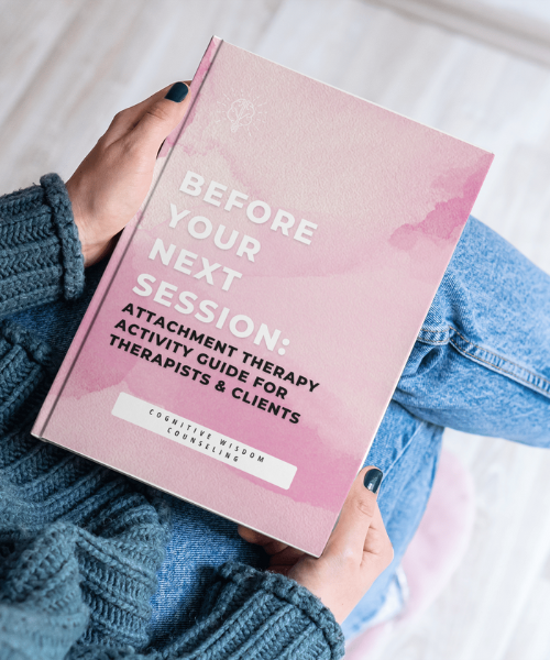 Person holding a book titled 'Before Your Next Session: Attachment Therapy Activity Guide for Therapists & Clients' with a soft pink cover. The book is designed to provide therapy activities related to attachment for both therapists and clients, published by Cognitive Wisdom Counseling.